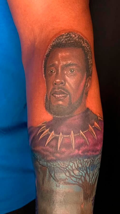 Close-up of a color tattoo depicting a man’s face with a gold necklace on an arm