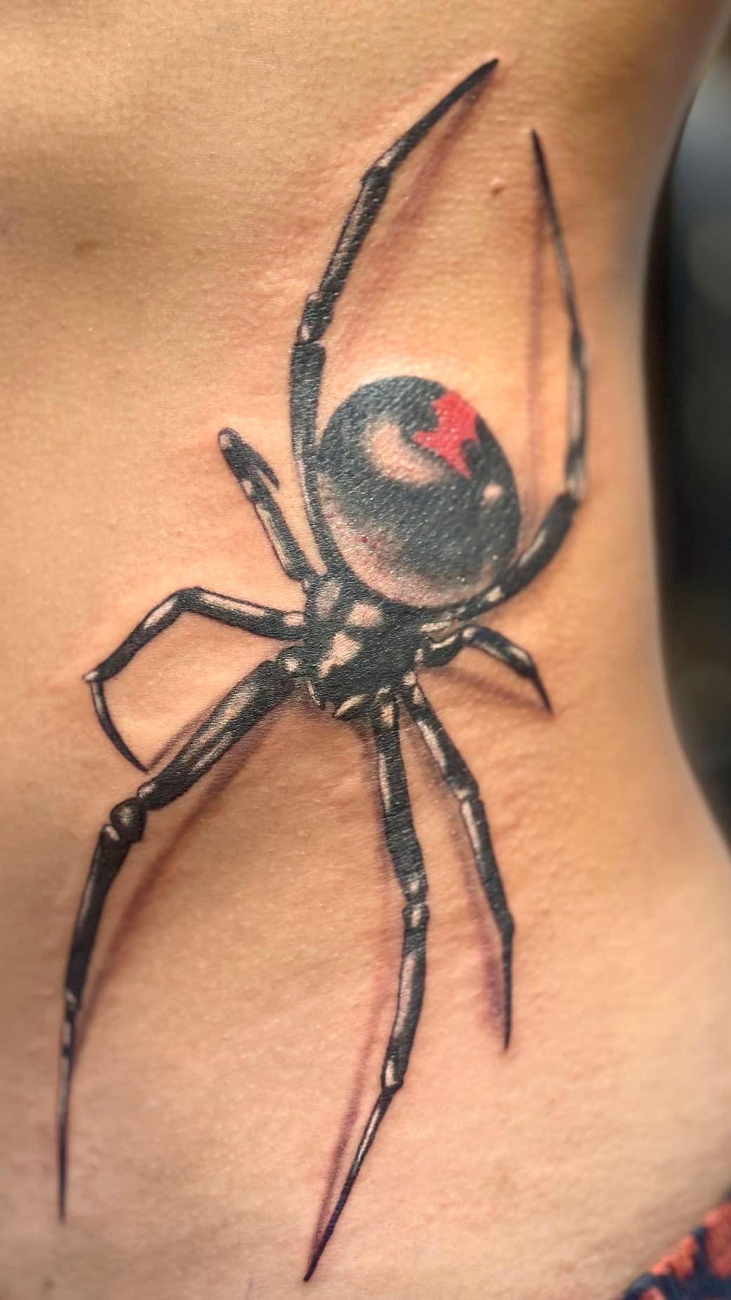 Black spider tattoo with red markings on skin