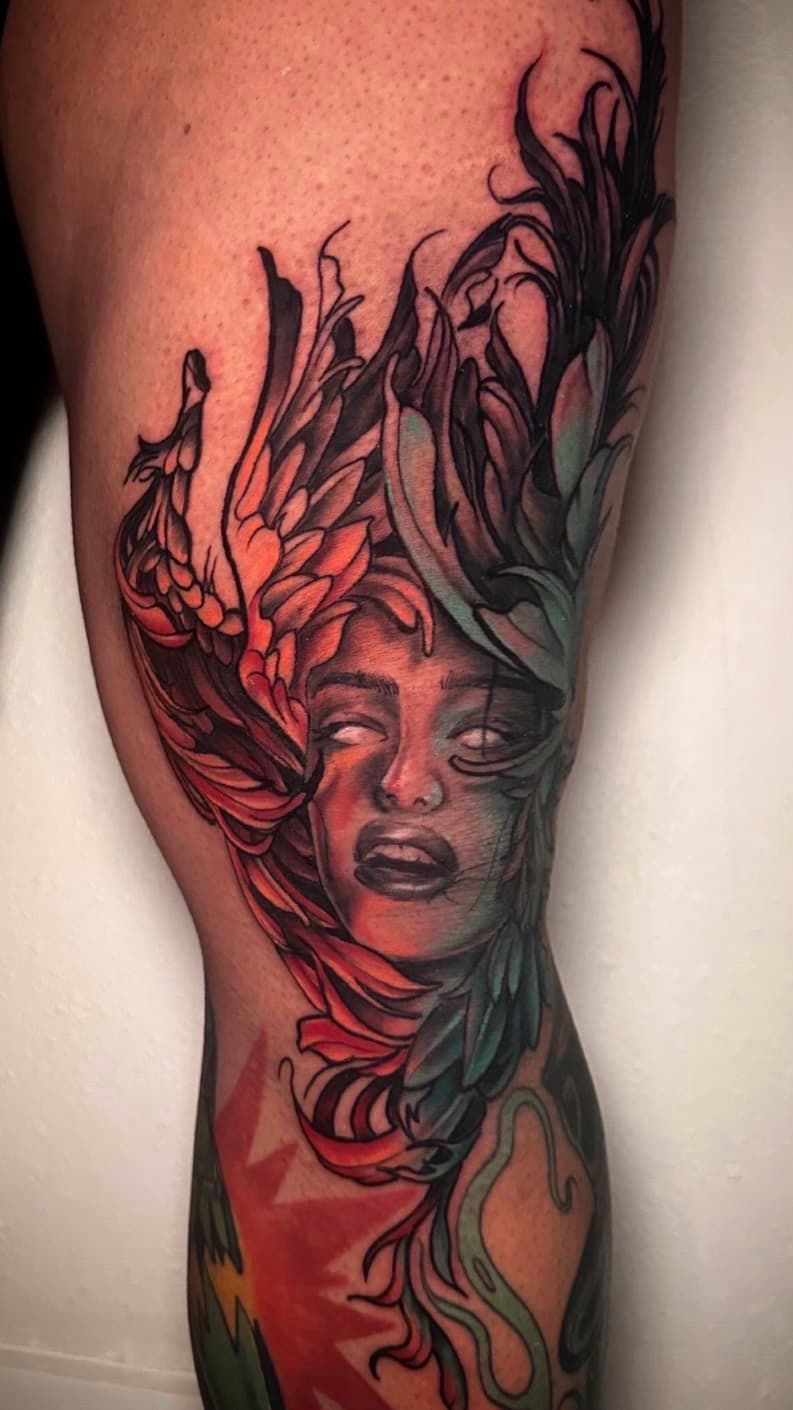 Detailed black-and-red tattoo of a woman’s face with flowing floral and leaf designs on a leg
