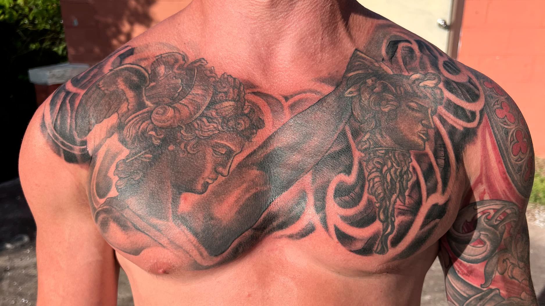 Close-up of a tattooed bare chest and shoulders with intricate black and red tribal-style designs