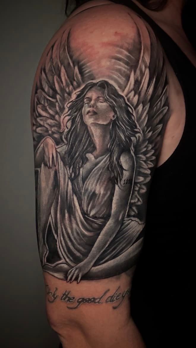 Winged angel tattoo on upper arm in grayscale with detailed face and robe, on a person’s shoulder