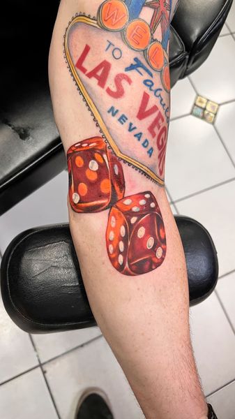 Lower leg with a Las Vegas tattoo and red dice on a black chair over white tile floor