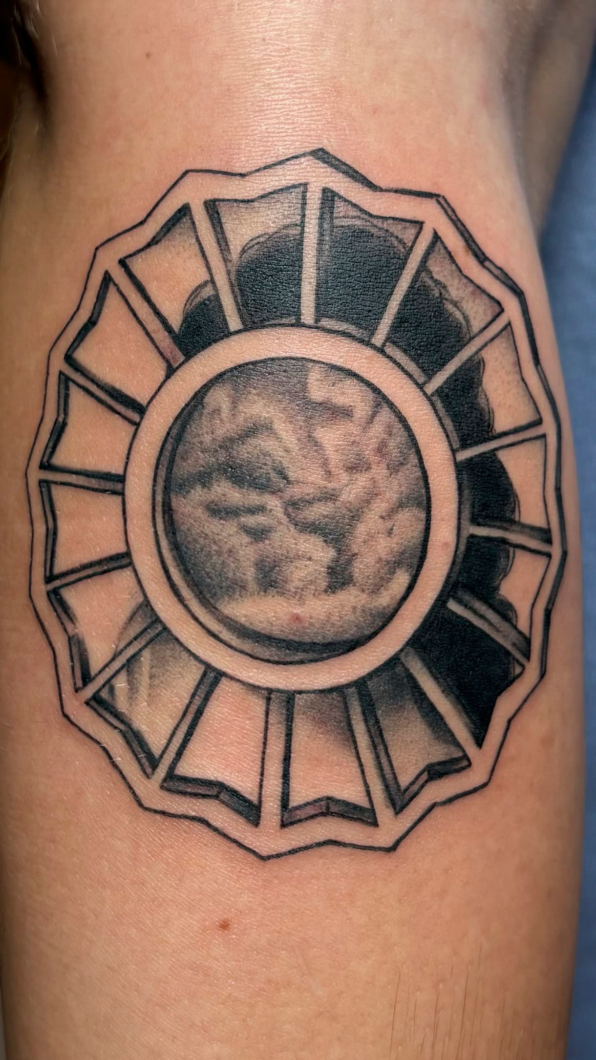 Black-and-gray geometric tattoo with a circular center on skin
