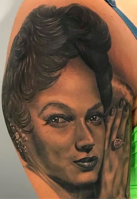 Portrait tattoo of a woman’s face with dark hair and hand, in black and gray shading.