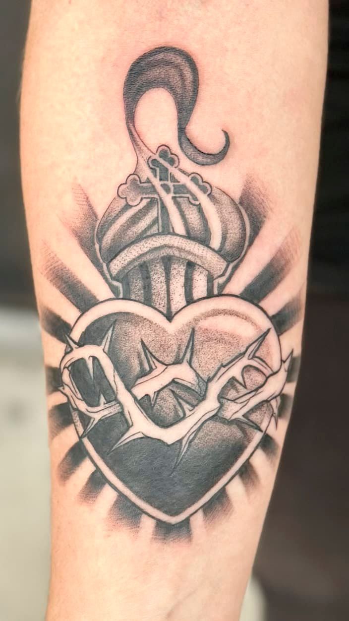 Black-and-gray tattoo of a heart with a sword and dagger, shaded with dramatic rays and a crescent above