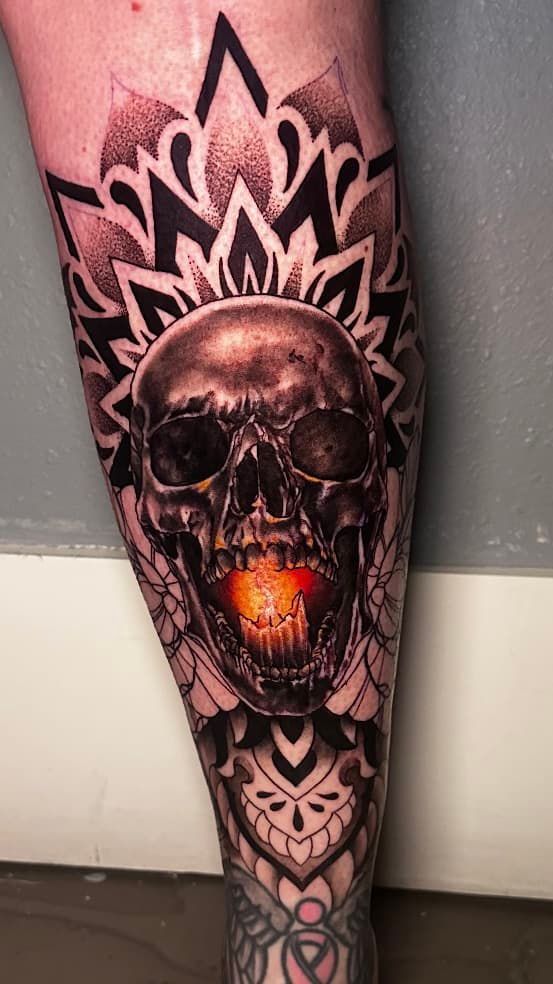 Black-and-gray skull tattoo with orange glowing mouth and geometric mandala pattern