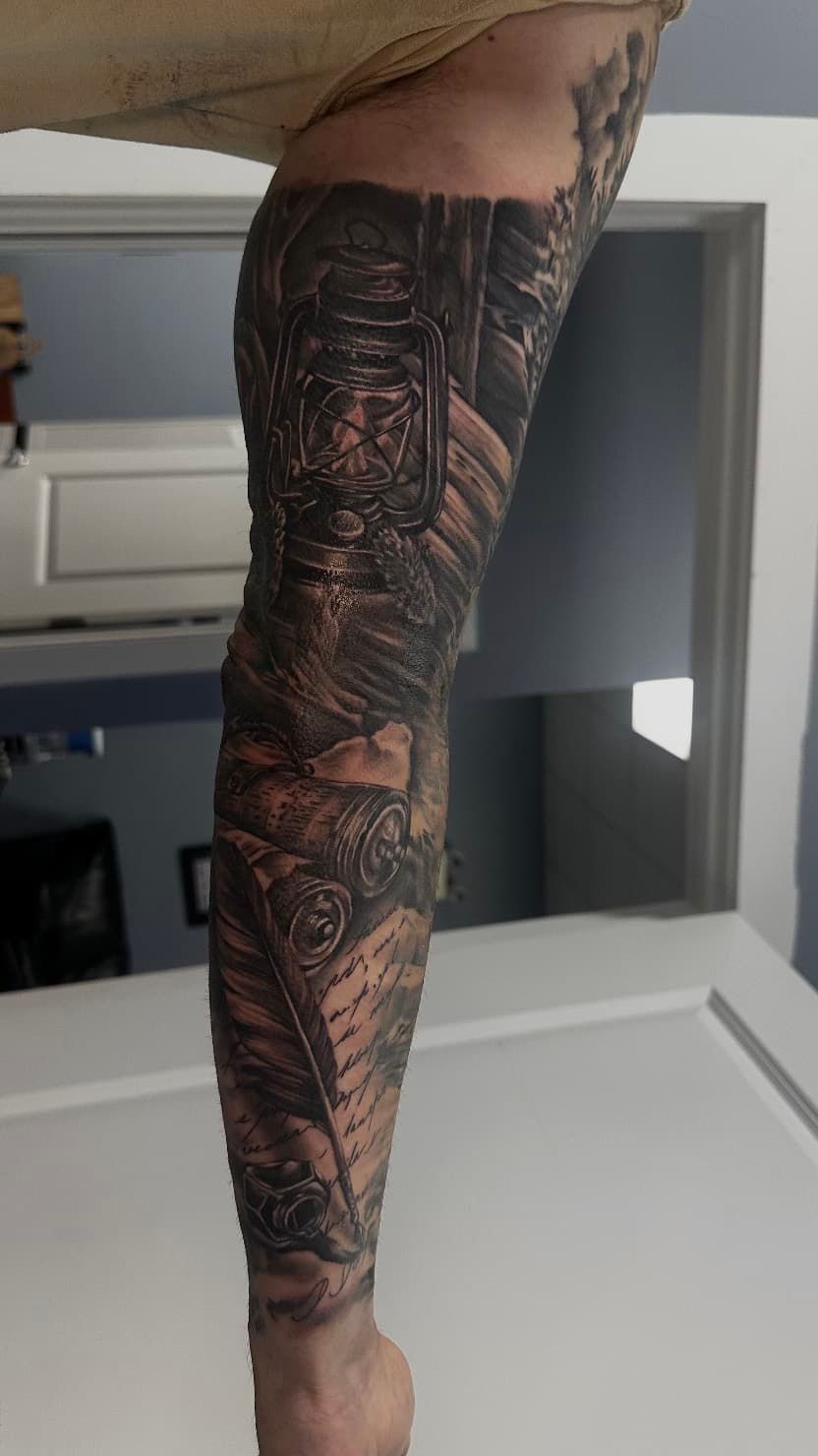 Arm with a dark, intricate sleeve tattoo from shoulder to wrist, shown in a room.
