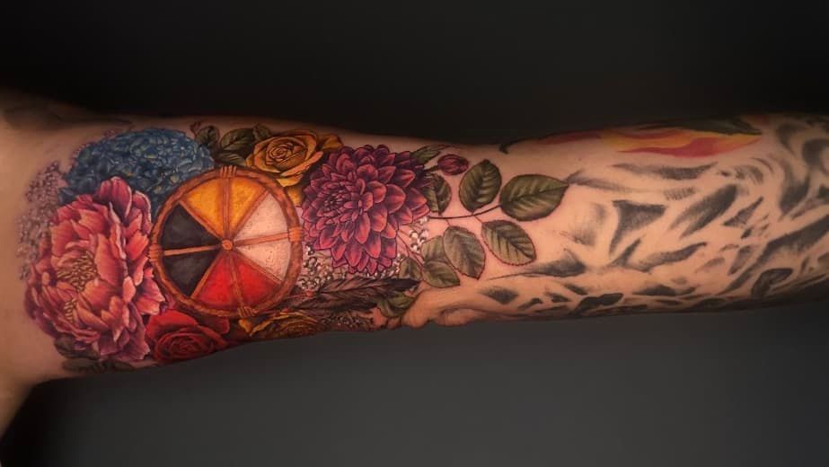 Colorful floral and geometric forearm tattoo in red, pink, orange, and black with leaf and feather designs