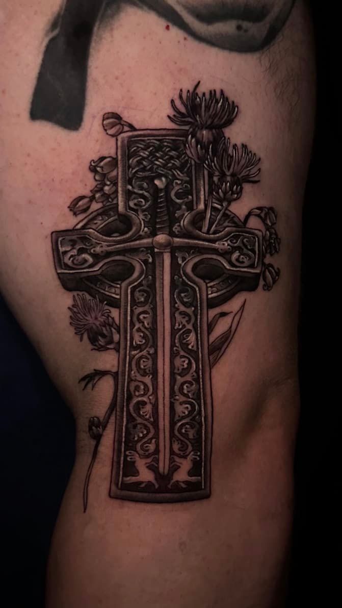 Close-up of an ornate black cross tattoo on a person’s upper arm.