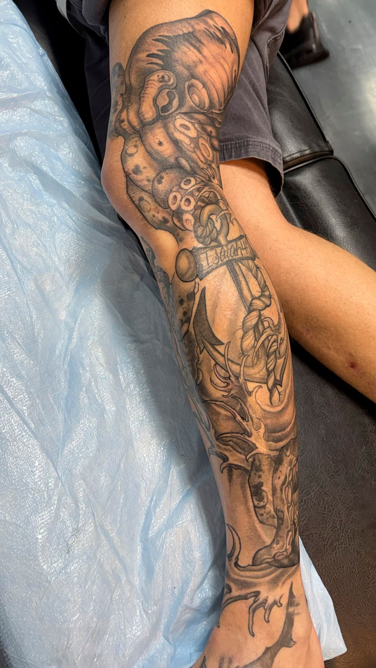 Arm tattoo sleeve with dark, intricate black linework on a forearm resting on a blue surface.
