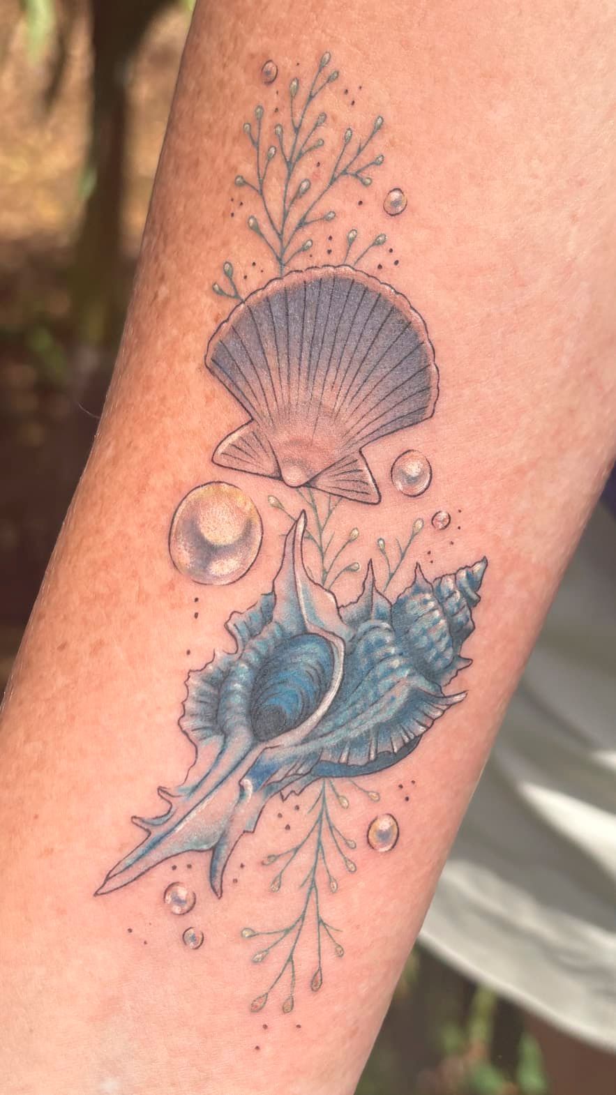 Blue shell tattoo on skin with delicate floral accents and two seashells.
