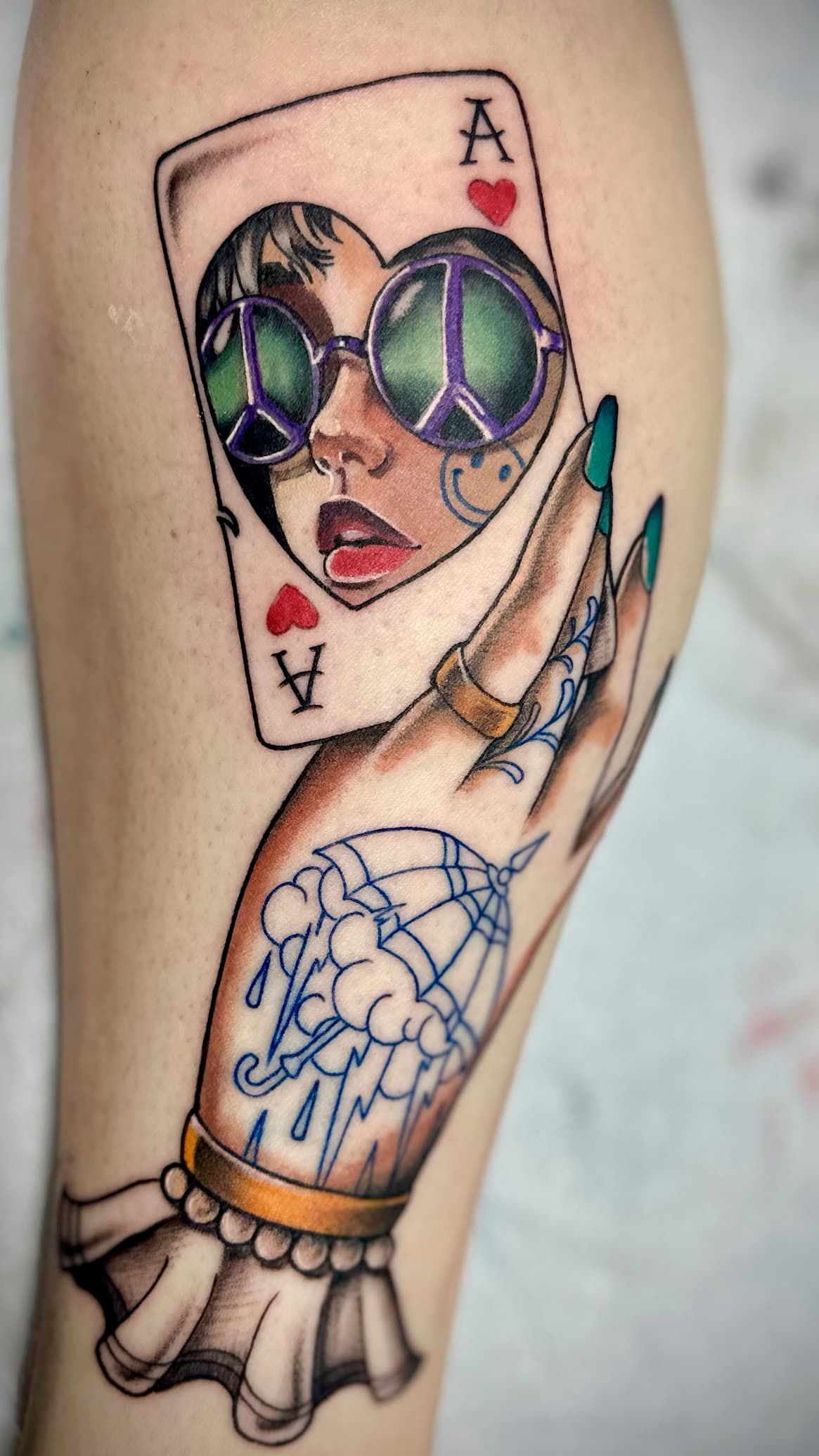 Card-themed arm tattoos: an Ace card face with colorful skull and a blue dreamcatcher on a hand.