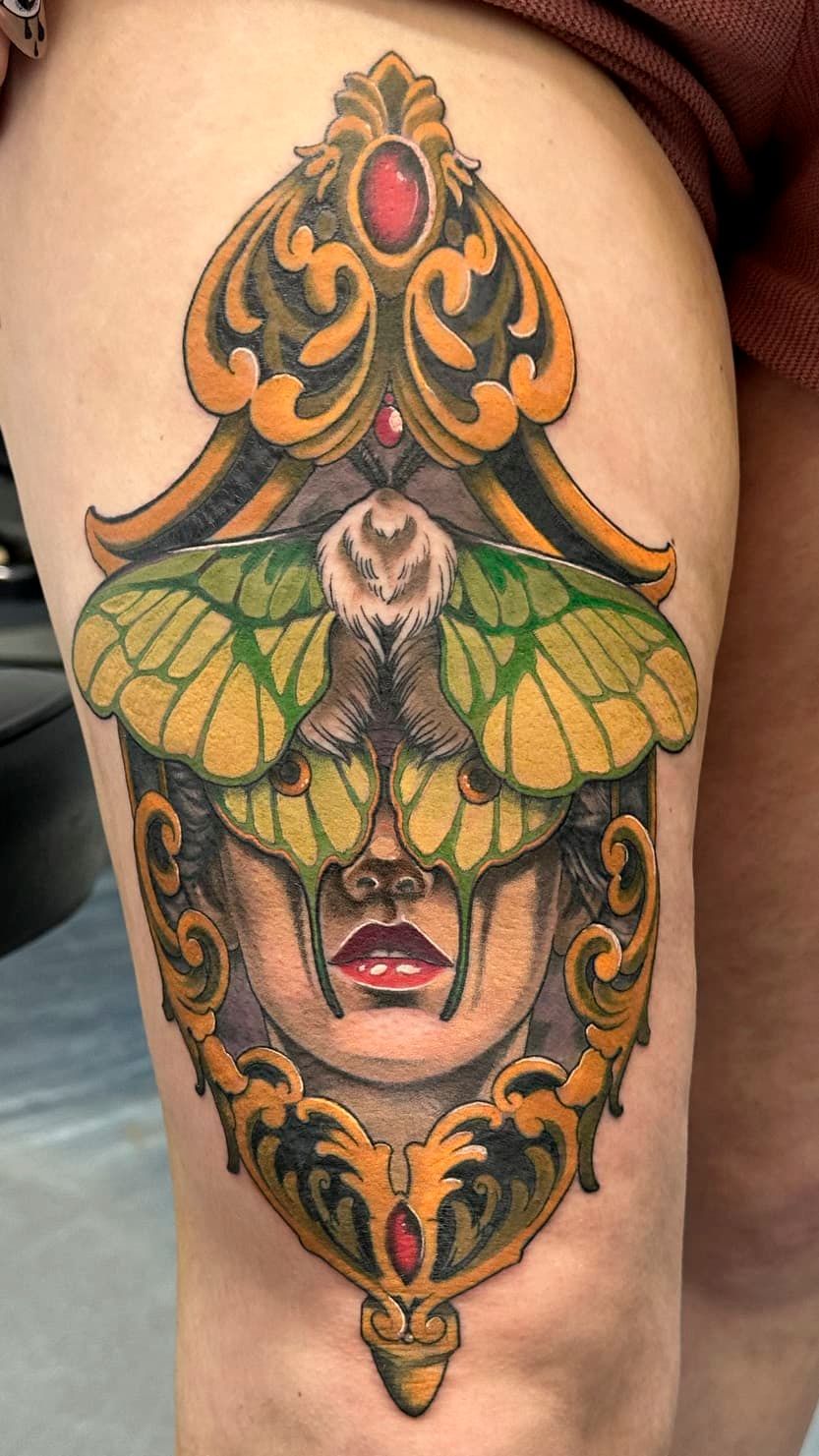 Colorful tattoo of a masked face with green butterfly wings and ornate orange-black decorative details on skin