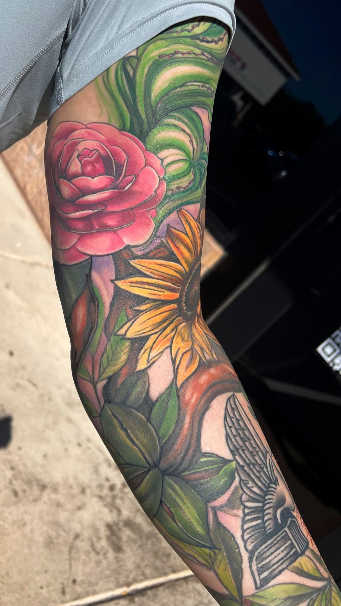 Forearm tattoo with a pink rose, yellow sunflower, and green leaves in vibrant color.