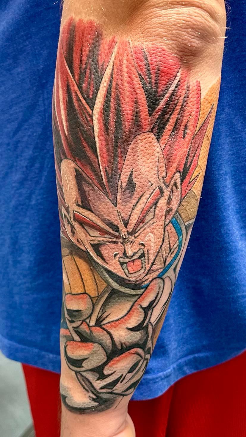Forearm tattoo of an intense anime fighter with spiky red hair and clenched fists on a blue shirt