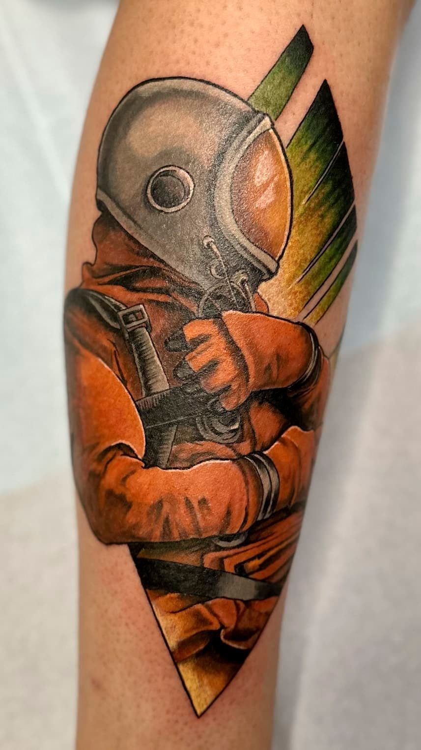 Tattoo of an astronaut in an orange suit with a gray helmet and green-orange background