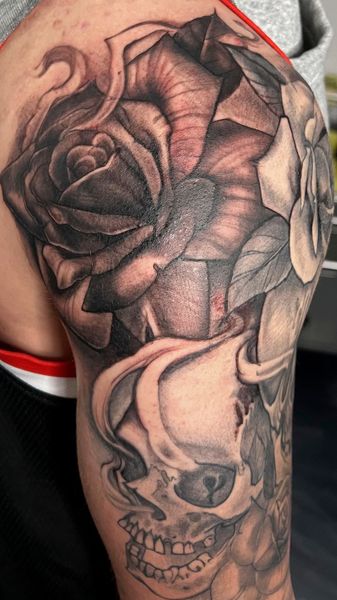 Close-up of an upper arm tattoo featuring a large black rose and a smoky skull design.