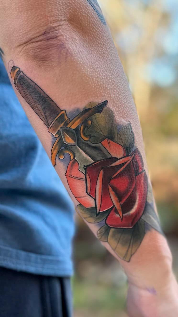 Forearm tattoo of a dark hand holding a red rose with black and orange accents