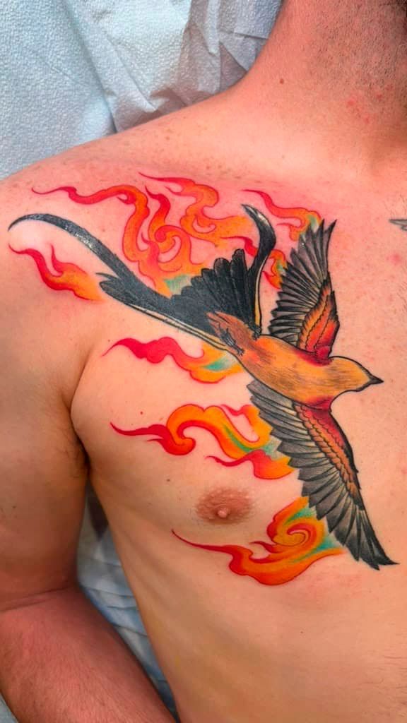 Colorful bird tattoo with flaming red, orange, and black wings on a bare upper chest
