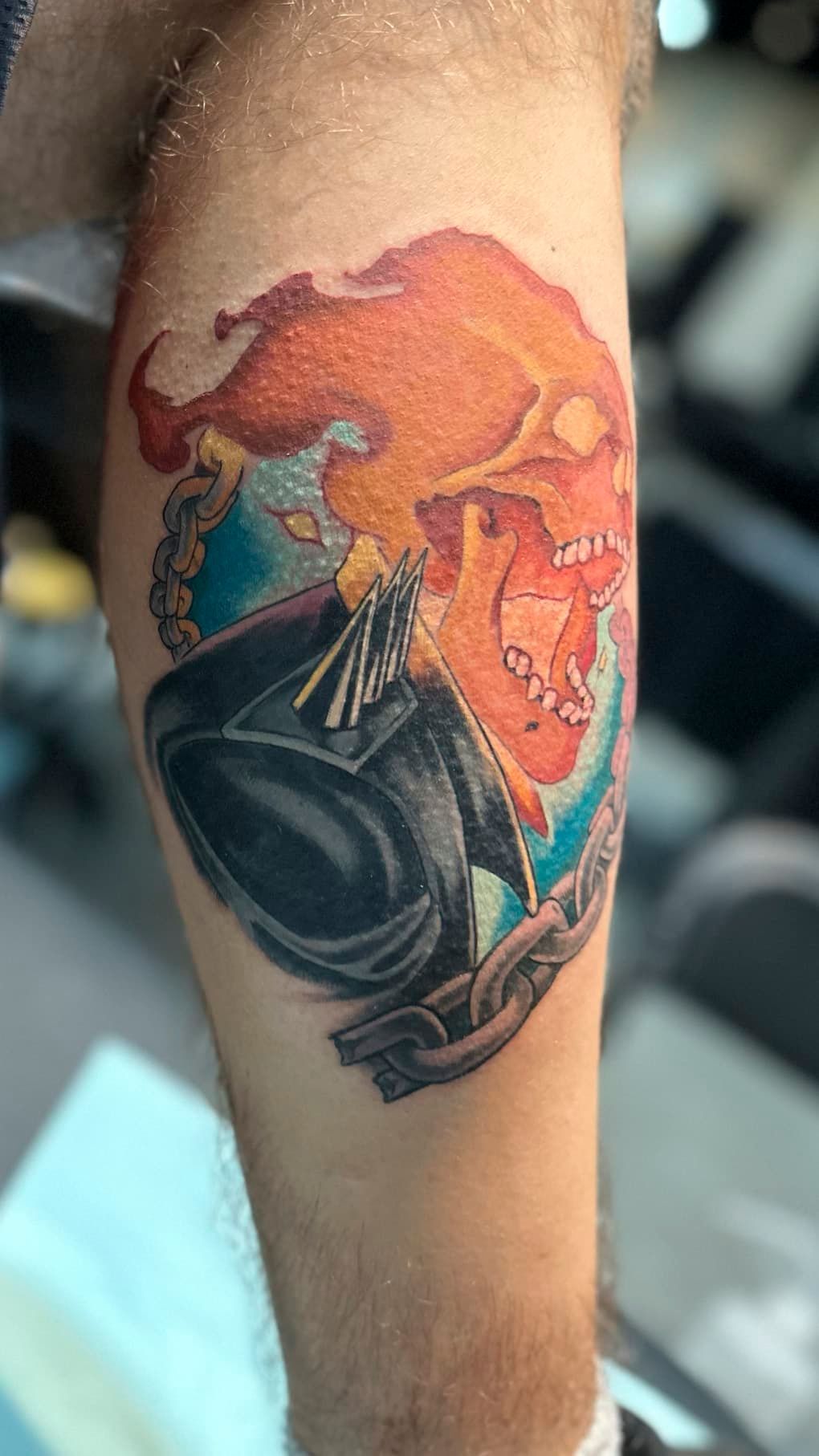 Colorful forearm tattoo of a flaming orange skull and black armored helmet on skin
