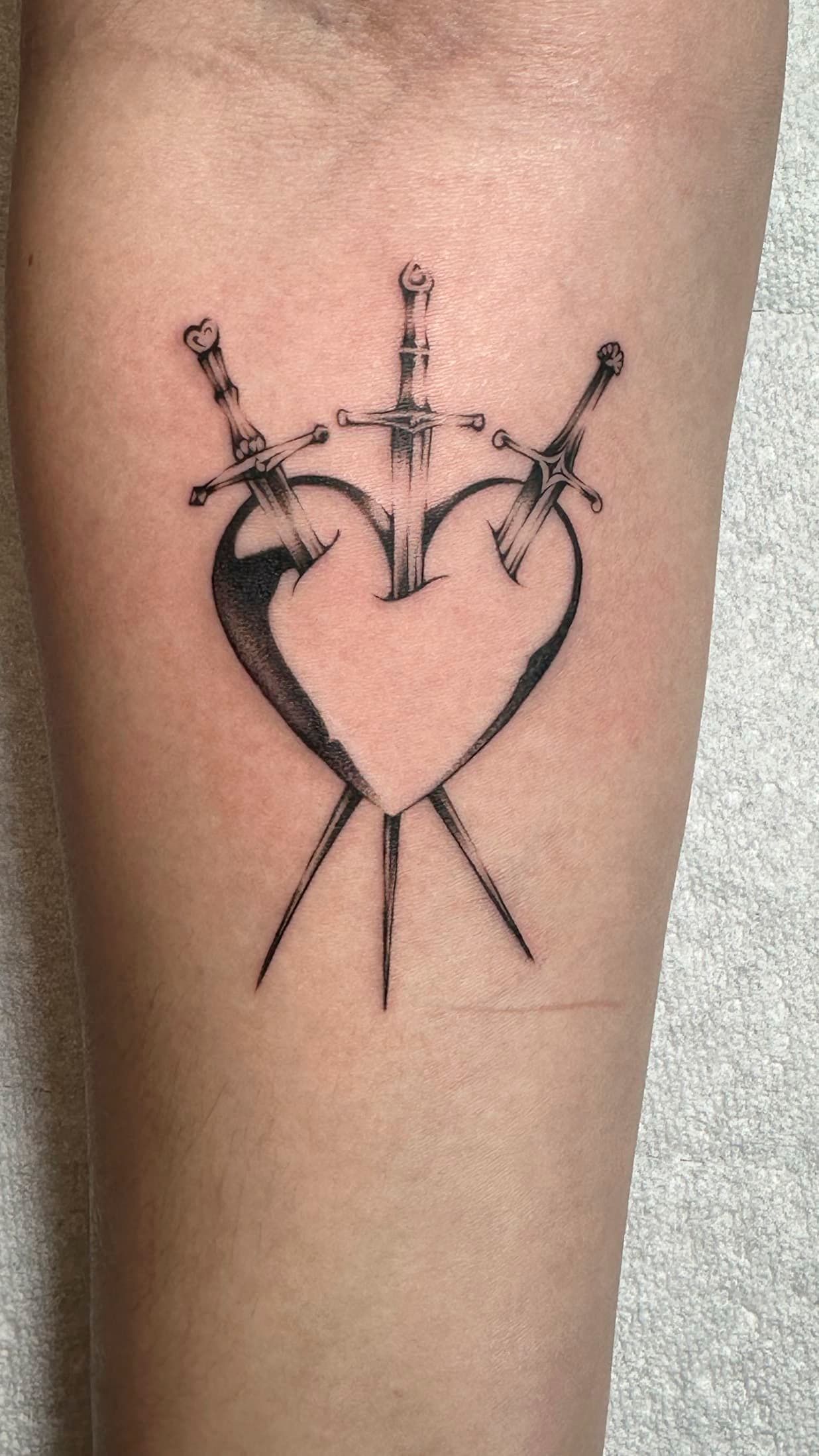 Black line-art tattoo of a crowned heart with crossed lines on skin.