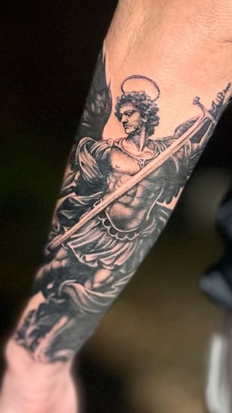 Black-and-gray tattoo of a robed figure with a halo on a forearm