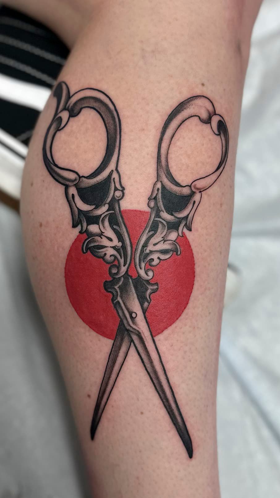 Scissors tattoo over a red heart on a person’s arm