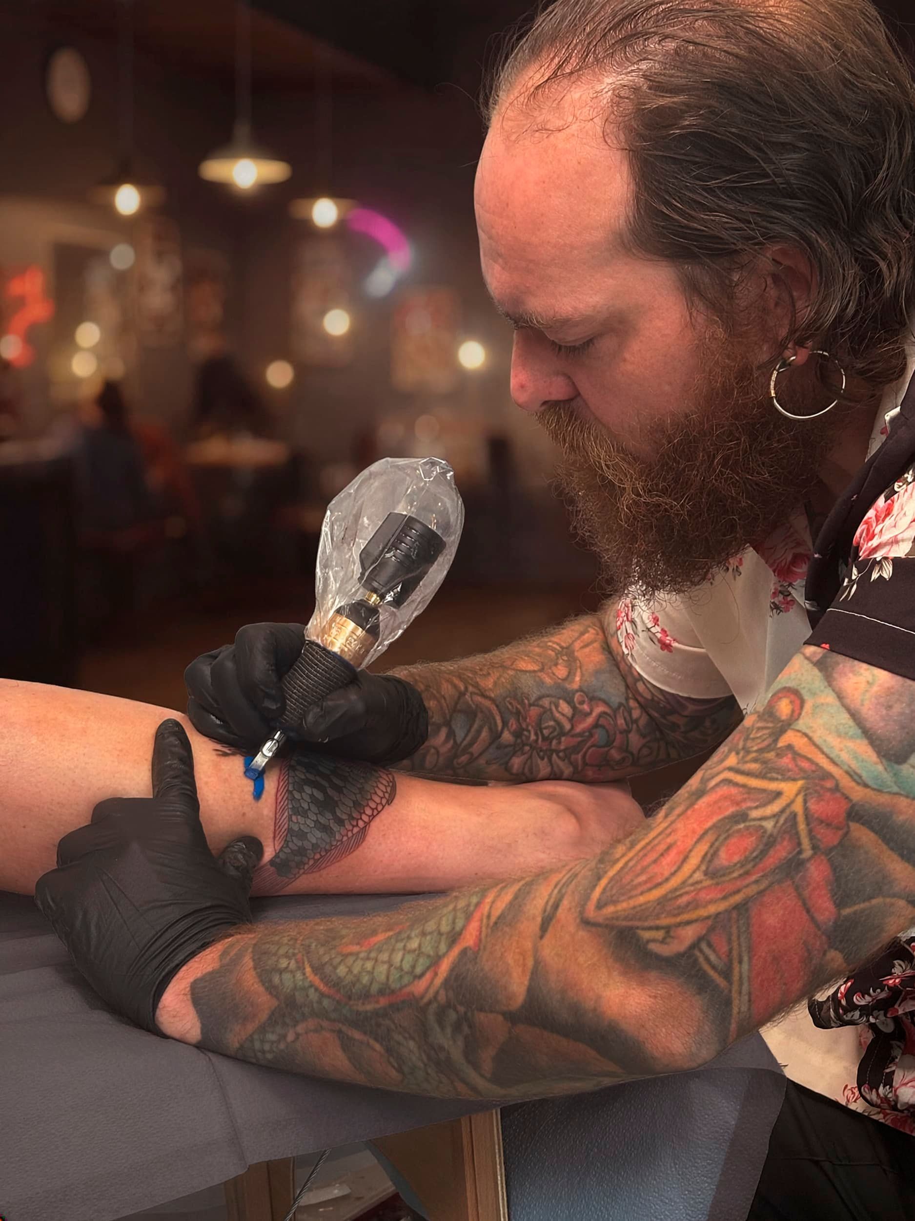 Tattoo artist using a machine on a client’s forearm in a dimly lit studio