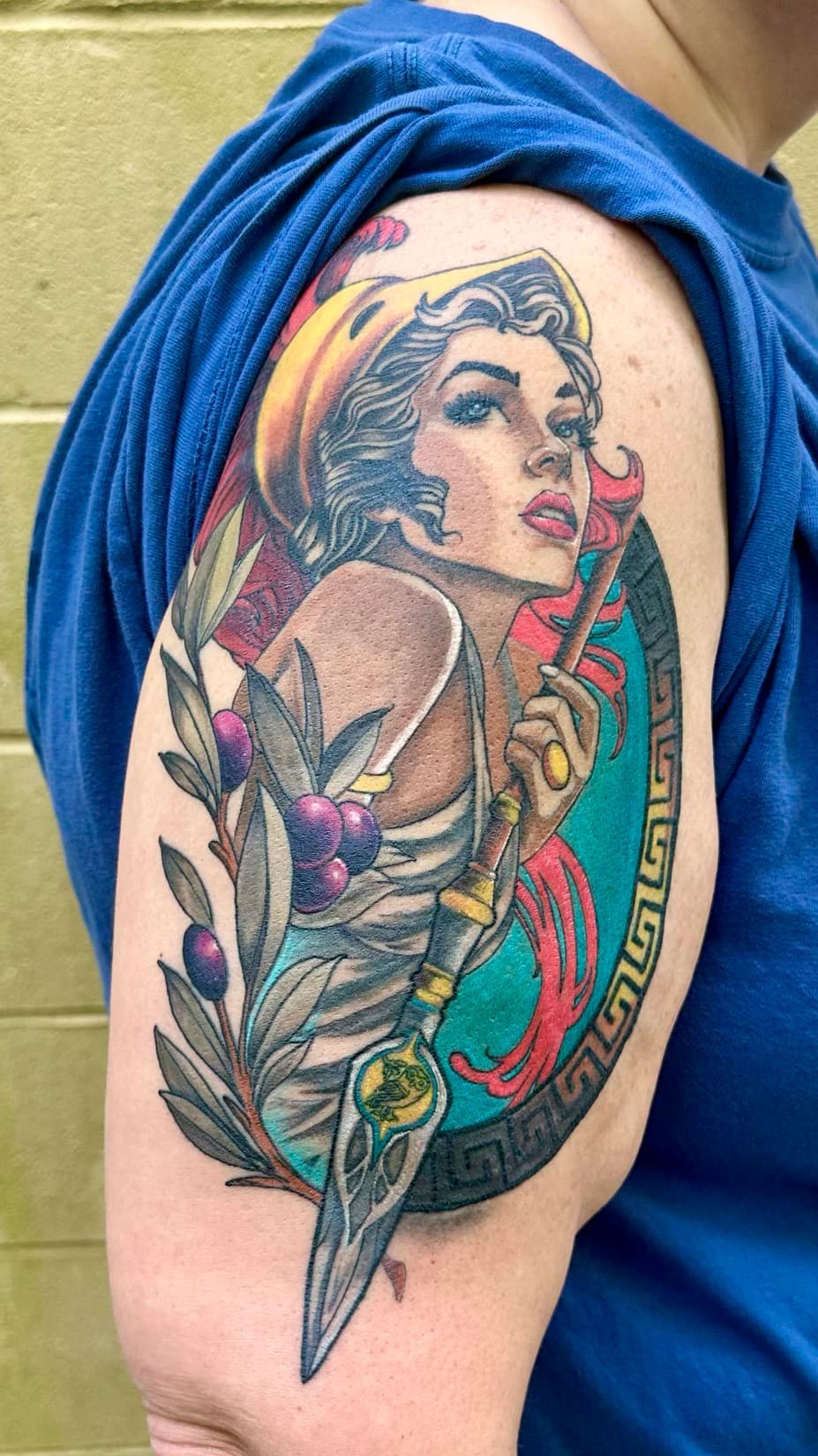Colorful tattoo of a woman’s face, rose, and dragonfly on an upper arm
