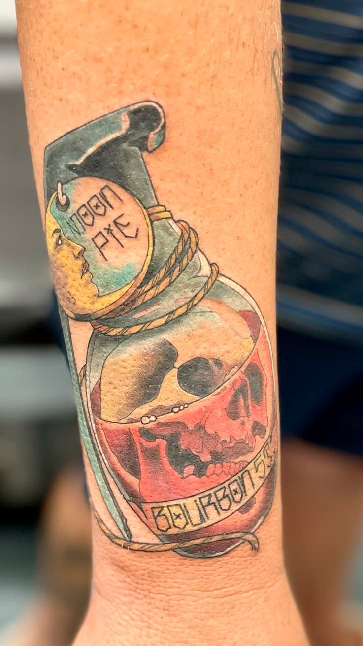 Forearm tattoo of a spray bottle labeled “Dawn Fight” with a skull illustration on the label