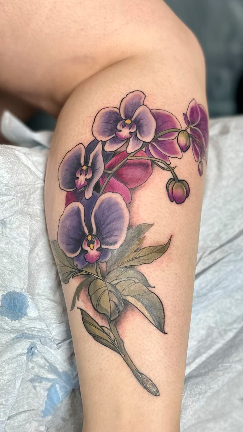 Purple floral tattoo on a bent arm with green leaves and small blossoms