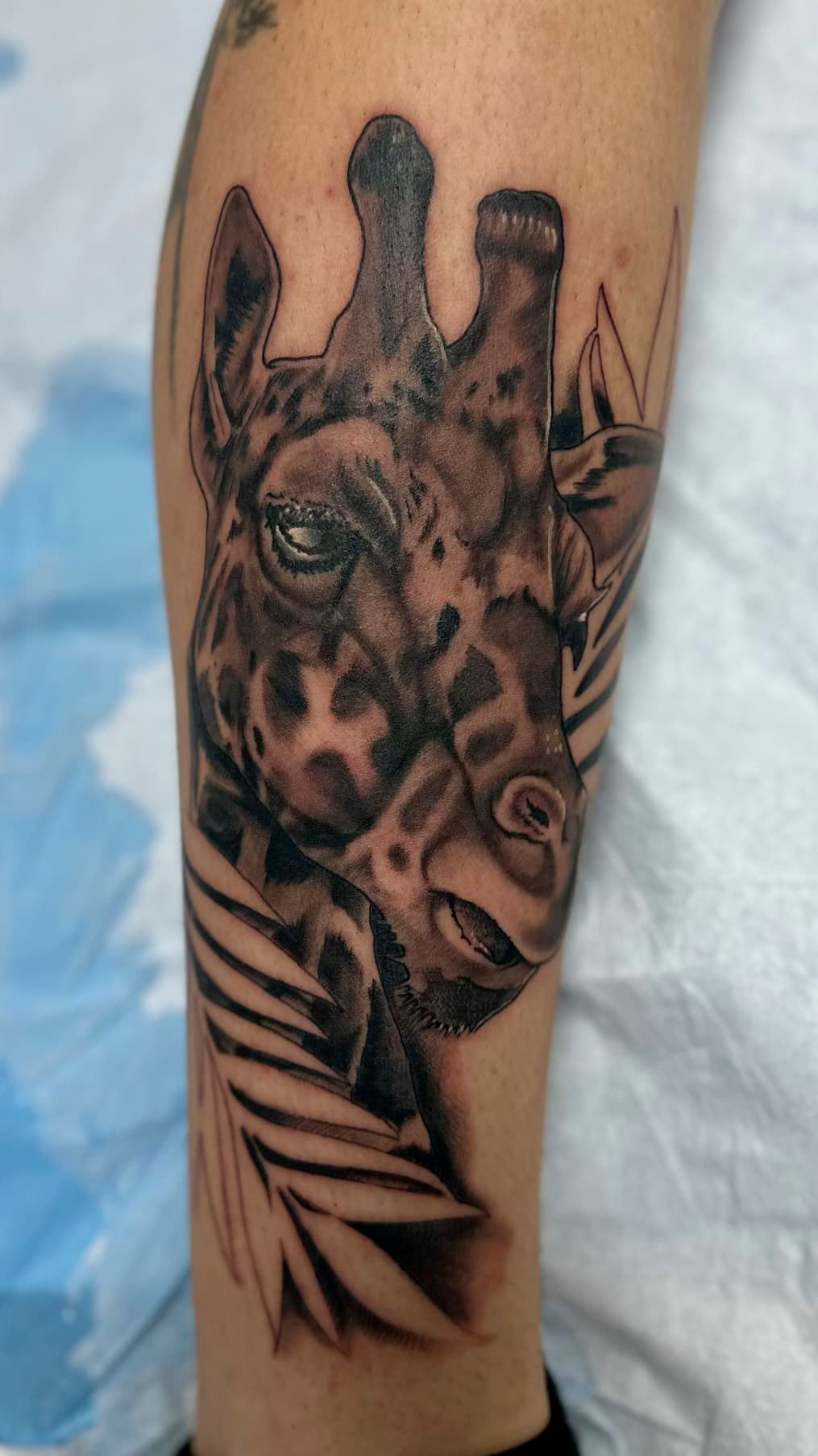 Giraffe tattoo on a forearm, with realistic brown and black shading and geometric accents