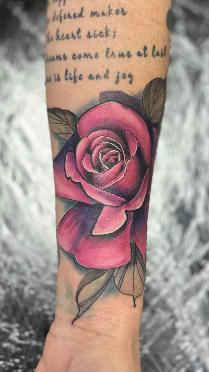 Pink rose tattoo on a forearm with leaves and script text above it