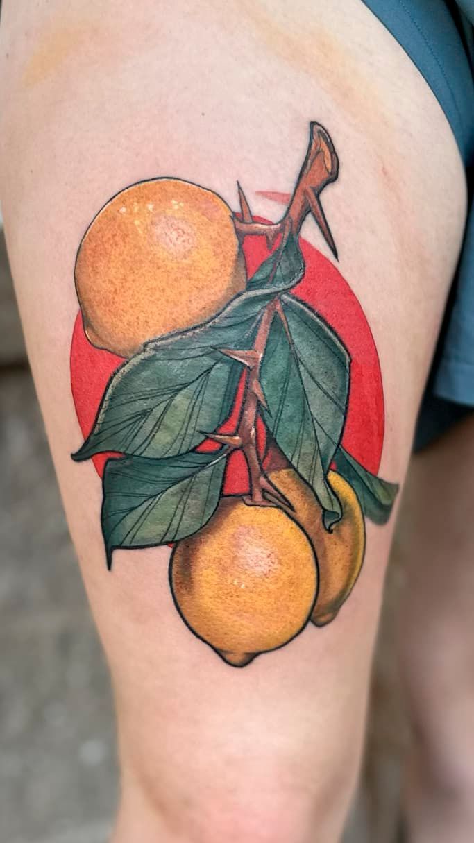 Colorful tattoo of oranges and green leaves on a person's upper arm