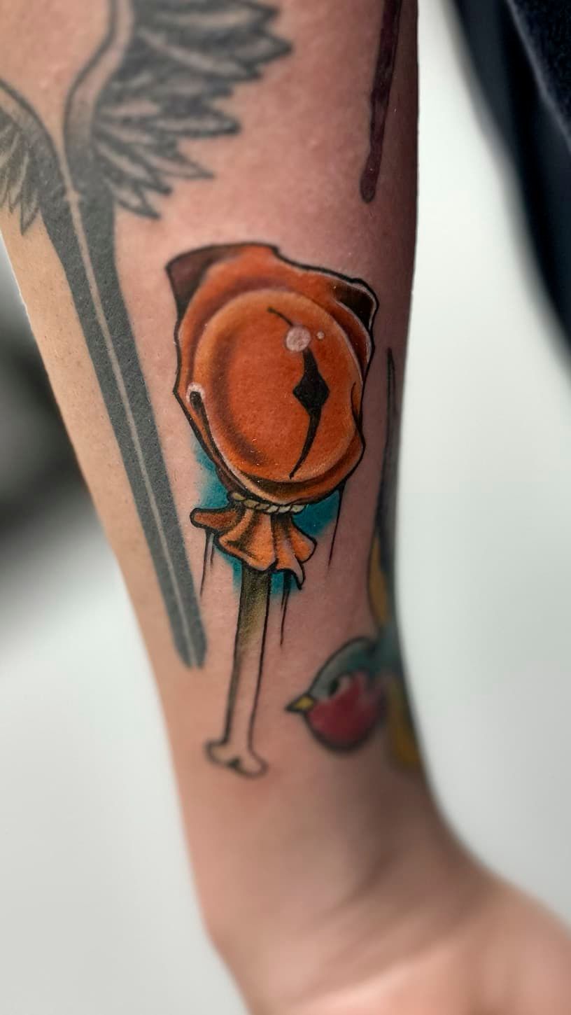 Colorful tattoo of an orange rose on a forearm with a small blue bow and red lips below