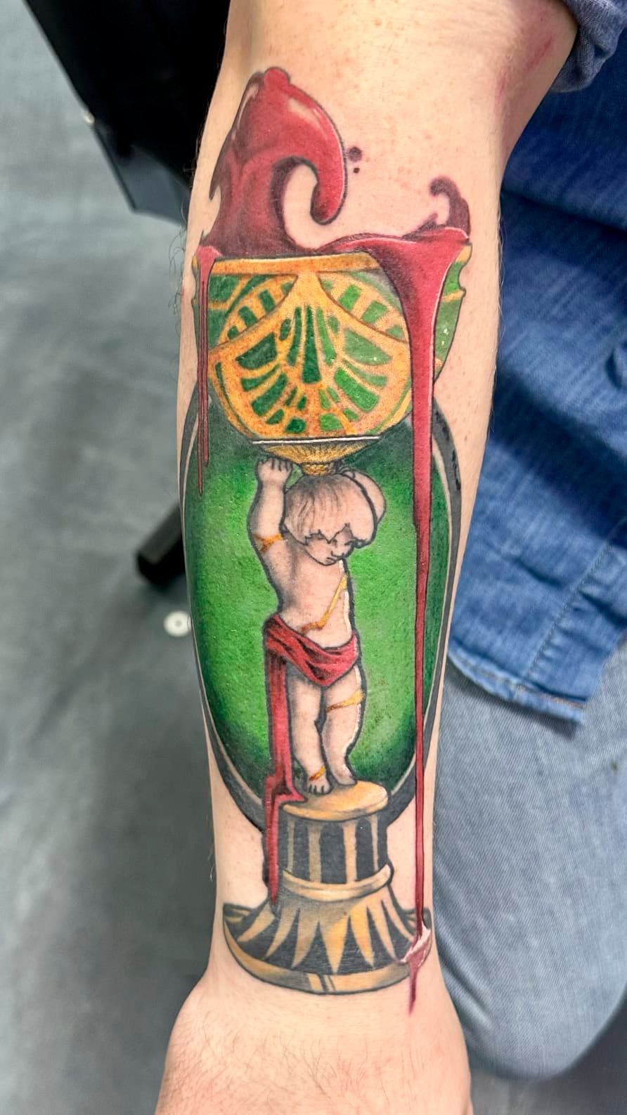 Colorful forearm tattoo of a bodybuilder under a barbell, with green, yellow, red, and black details.