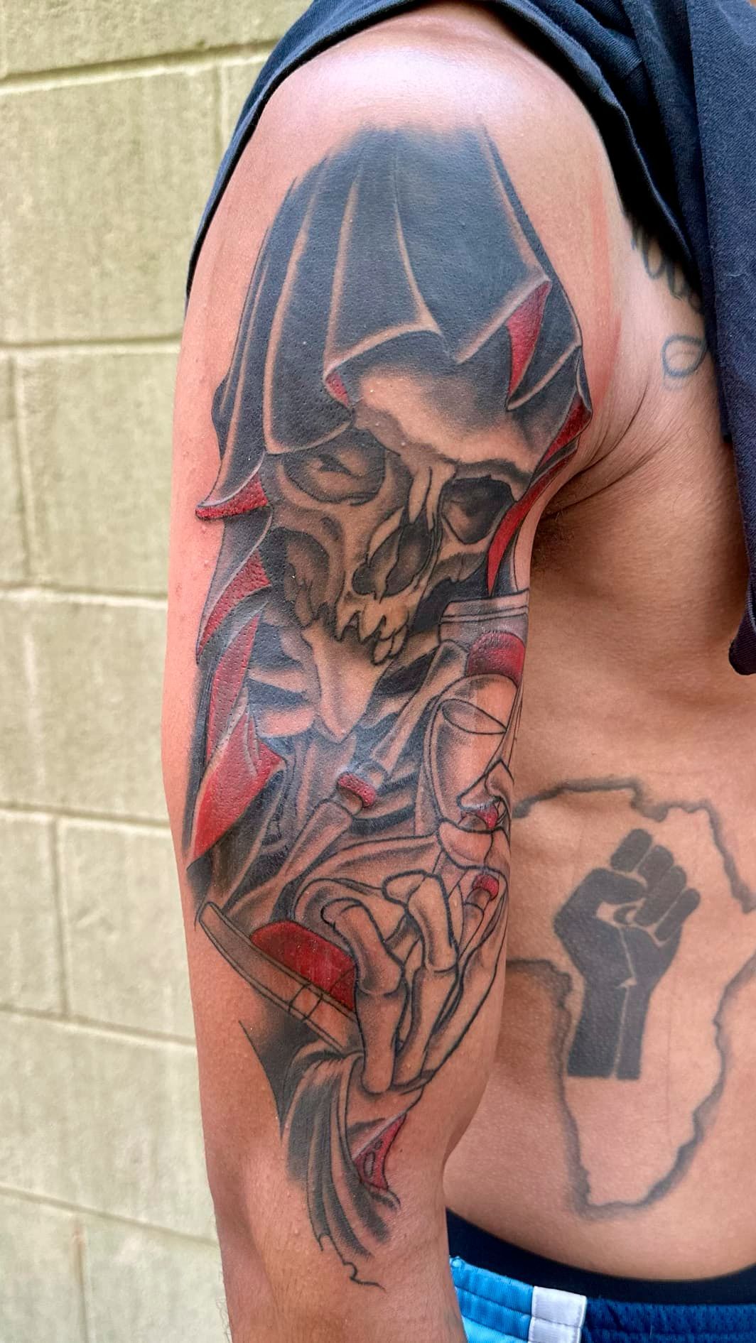 Close-up of a man’s upper arm and side with a large red-and-black demon tattoo