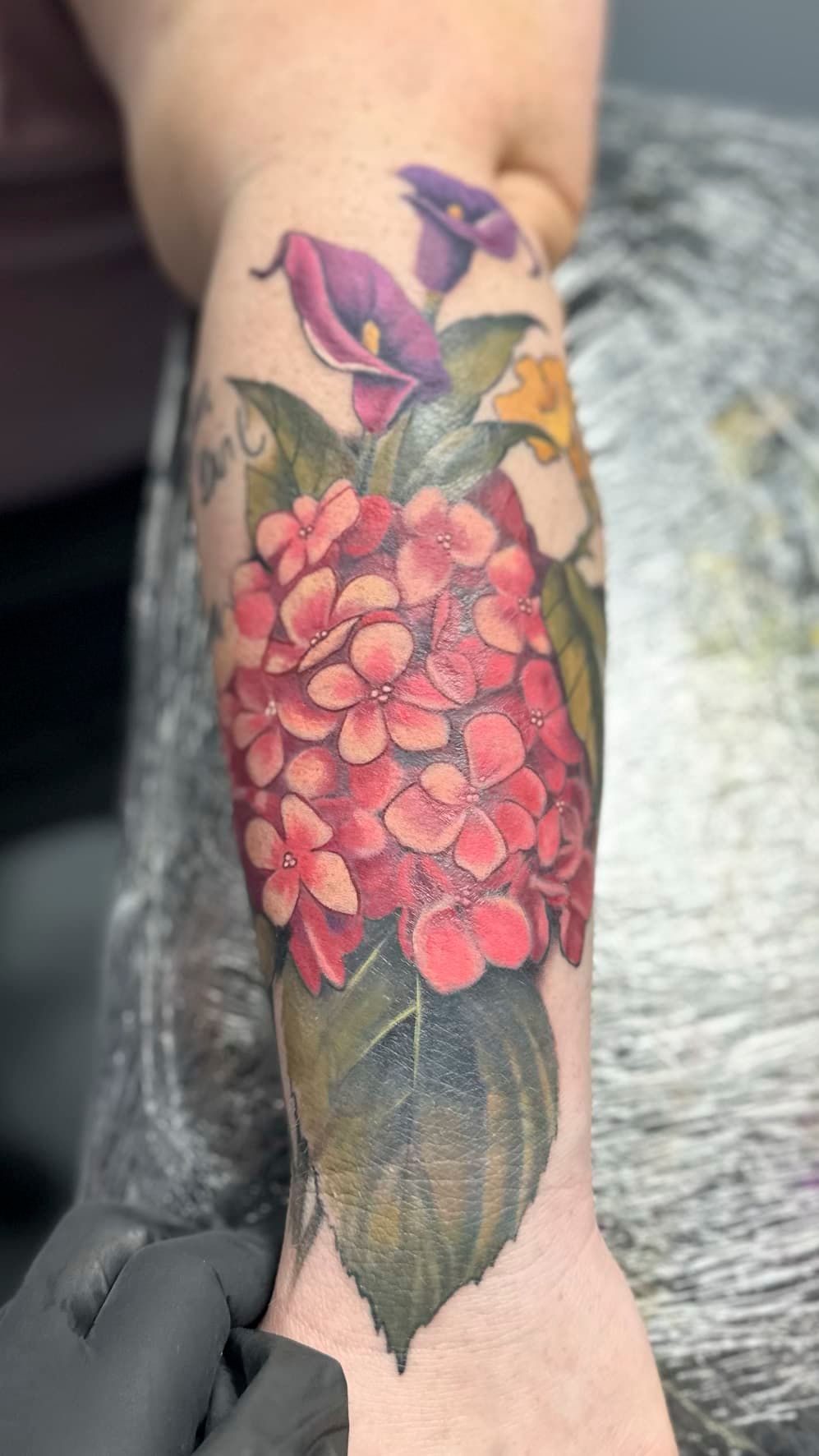 Colorful floral tattoo on an ankle and lower leg, featuring pink blossoms and purple flowers