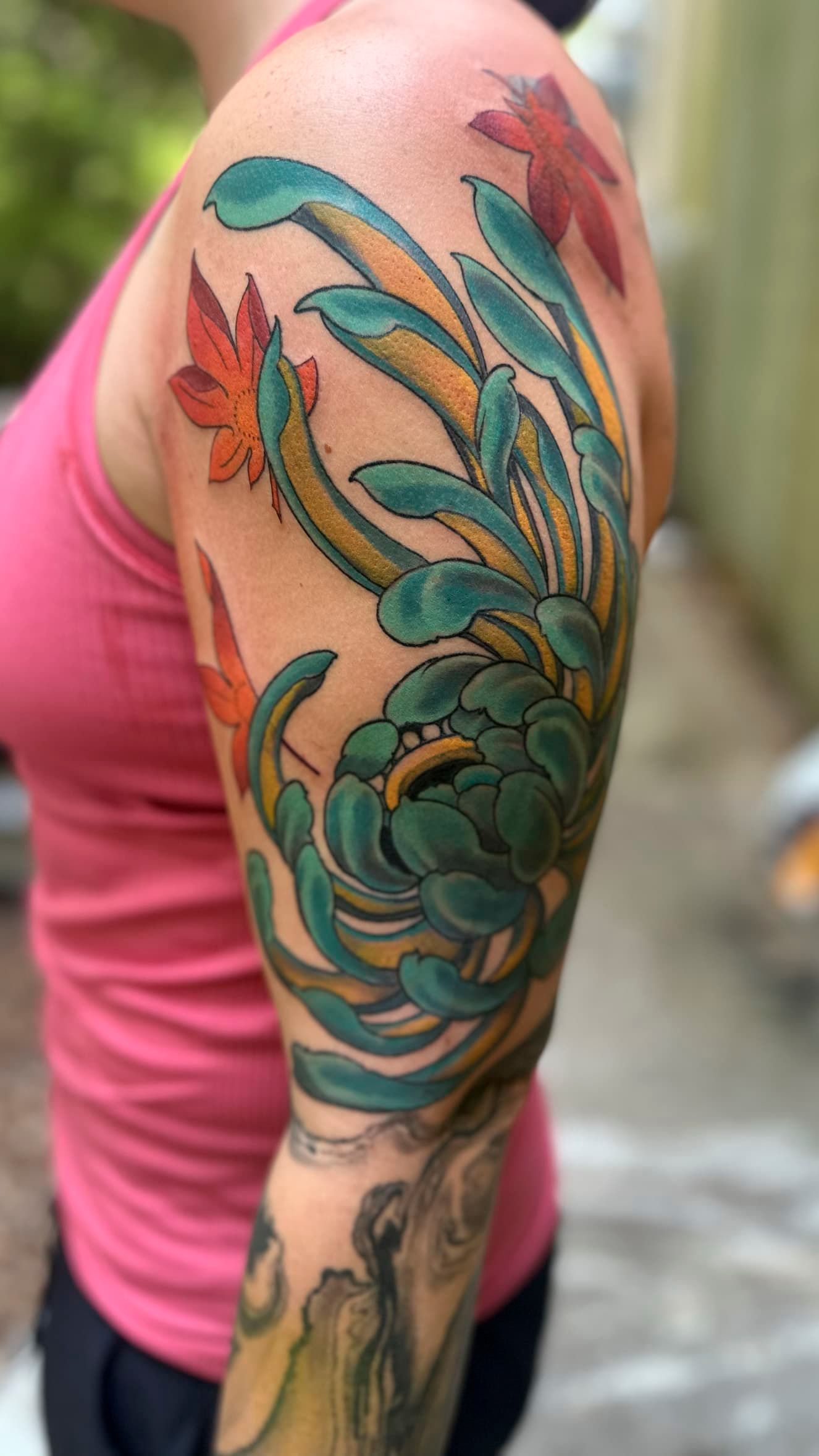 Close-up of a colorful teal, orange, and pink floral tattoo on a person’s upper arm and shoulder