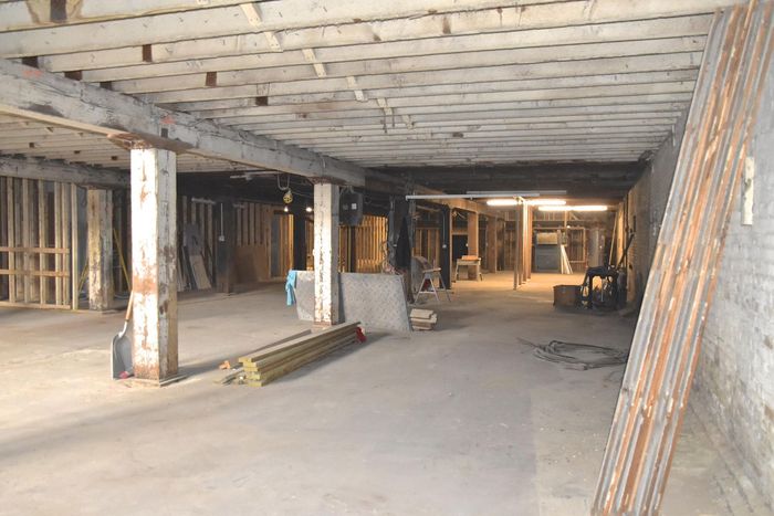 Un cantiere edile al coperto ancora incompiuto, con pavimenti in cemento, travi a vista e colonne portanti.