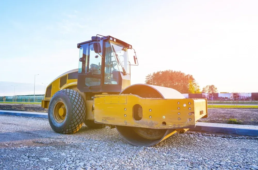 Yellow road roller compacting gravel on a construction site under a bright sky. — Allquip Rentals Pty Ltd in Cooroy, QLD