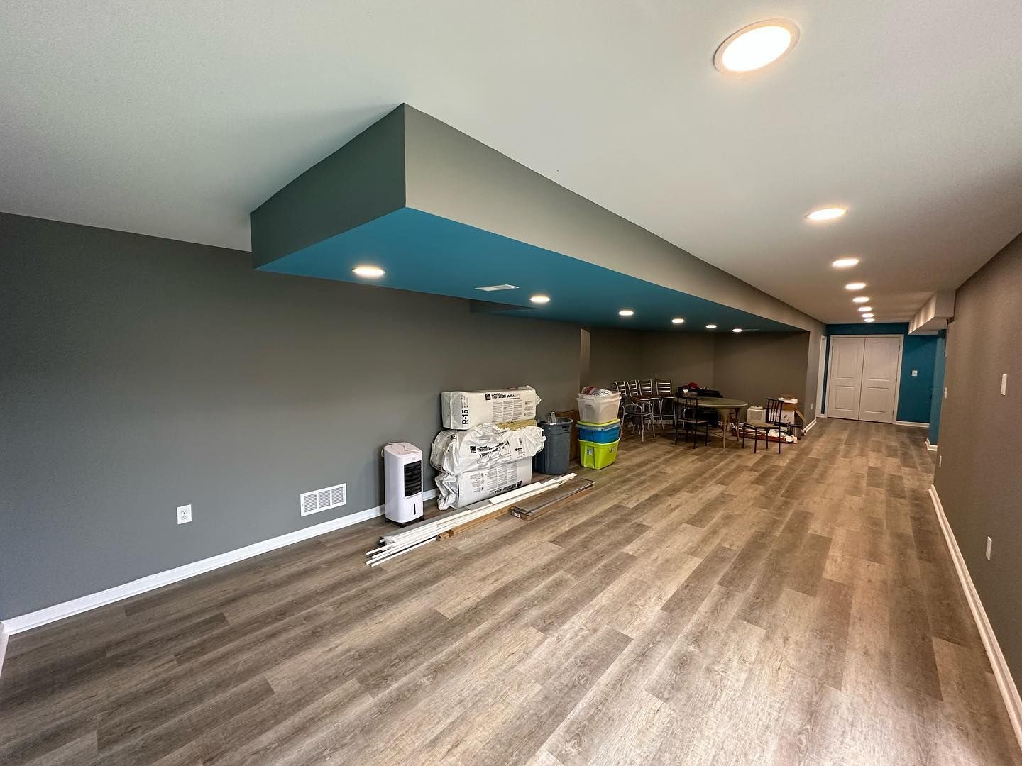 Basement with gray walls, wood-look flooring, and a blue ceiling section. Items against walls.