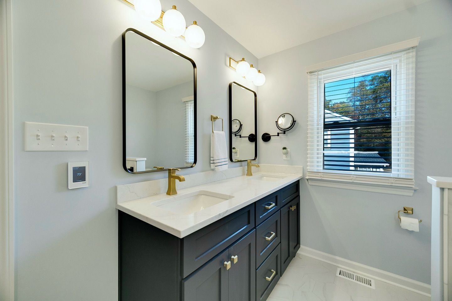 A bathroom with two sinks , two mirrors and a window.