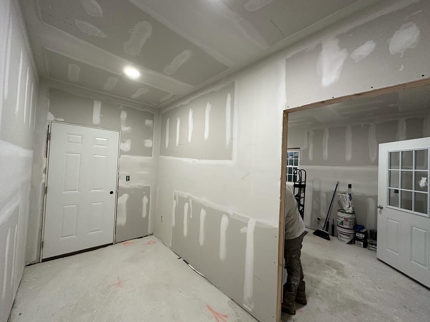 A man is standing in a room with drywall on the walls.