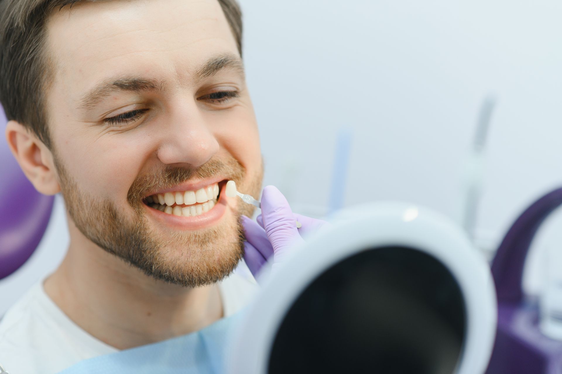 Man smiling as a dentist examines his teeth with a mirror in a bright clinic