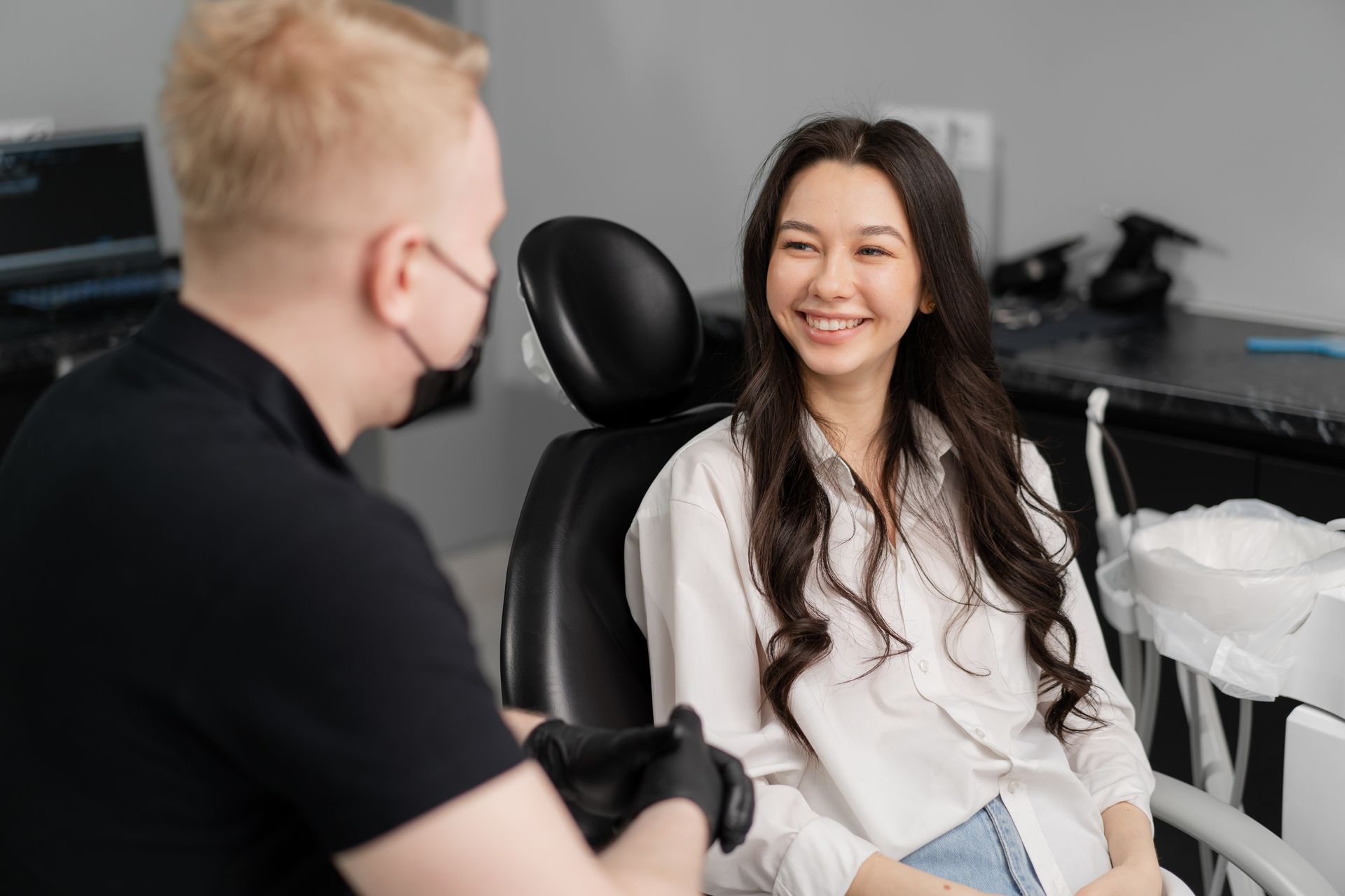 Two people chatting in a dental office, one smiling in a chair with equipment nearby