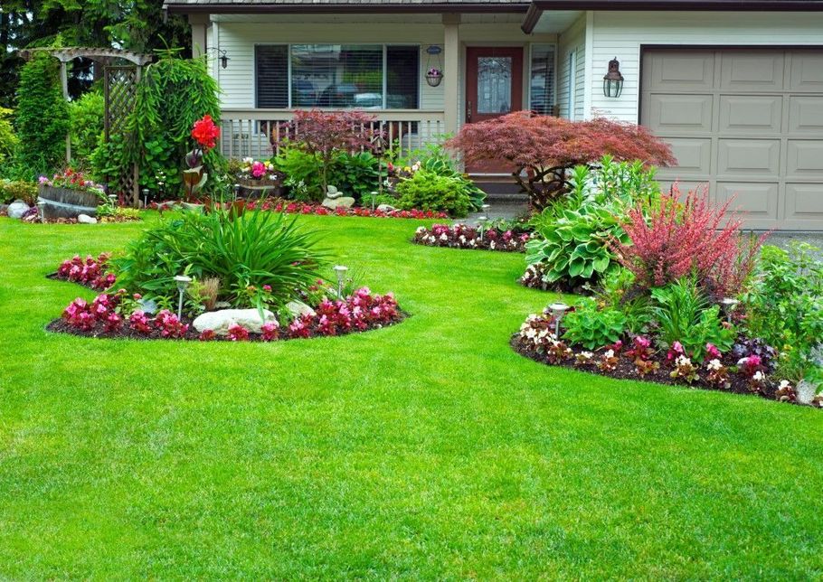 Front yard garden with colorful flower beds and a lush green lawn in front of a house and garage
