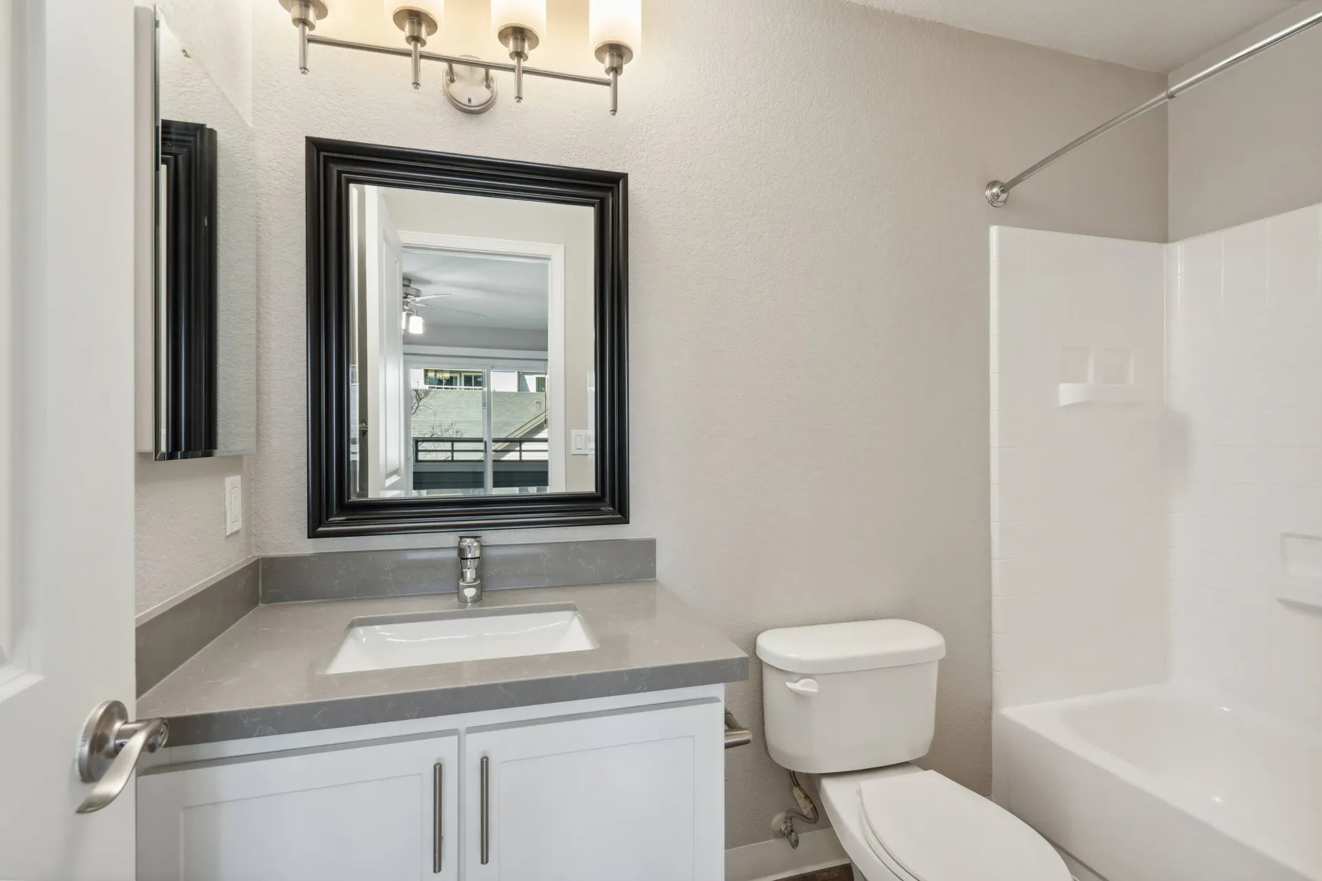 Bathroom in an apartment with gray countertop, white vanity, mirror, toilet, and tub/shower at The Reserve at Capital Center.