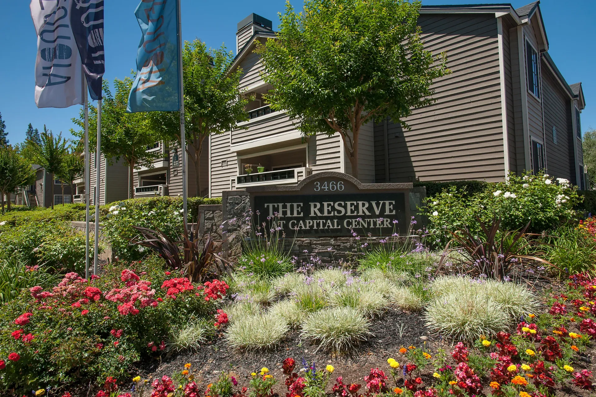Exterior view of a multifamily community entrance with landscaping and a stone sign at The Reserve at Capital Center.