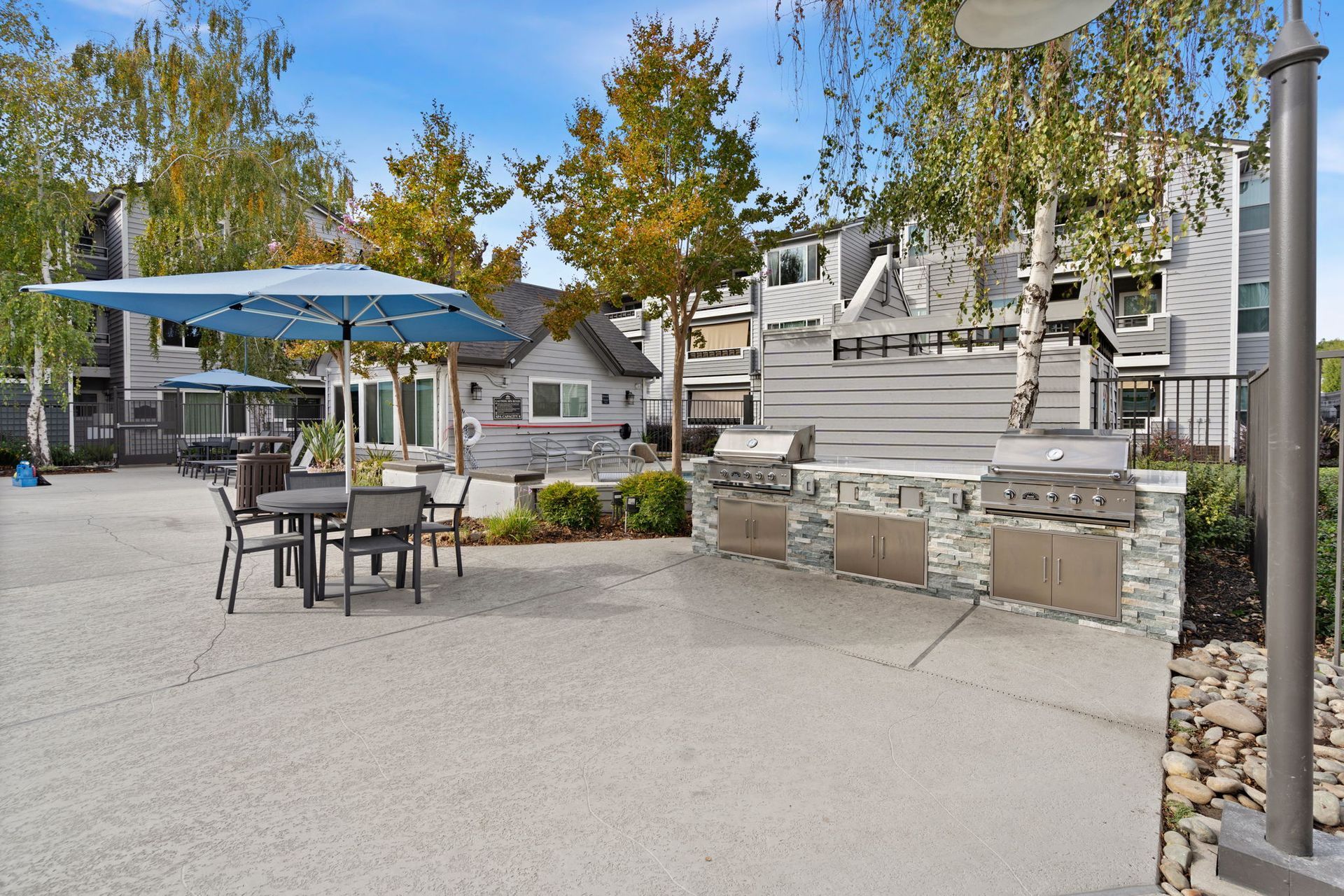 Outdoor community barbecue area with grills, tables, and blue umbrellas  at The Reserve at Capital Center.